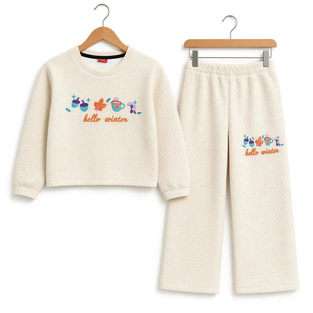 A two-piece children's lounge set consisting of a cropped long-sleeve top and matching pants, both in a textured cream waffle fabric. The set features a colorful graphic of winter-themed icons (snowman, scarf, hat, gloves, sunglasses) above the text 'hello winter' in orange.