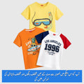 Three kids' short-sleeve t-shirts displayed together on a light gray background: a yellow shirt with a snorkel and goggles graphic, an orange shirt with a tropical beach graphic and text, and a white raglan shirt with navy sleeves and 'LOS ANGELES 1996' text. A blue banner with Urdu text is at the bottom.