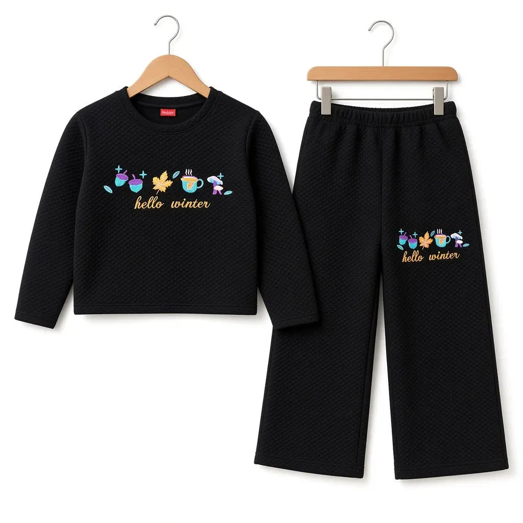 A two-piece children's outfit set consisting of a black textured long-sleeve top and matching black cropped pants, both hanging on wooden hangers against a white background. The top and pants feature a colorful graphic of winter-themed characters (snowman, carrot, snowman, snowman, snowman, snowman) above the gold text 'hello winter'.
