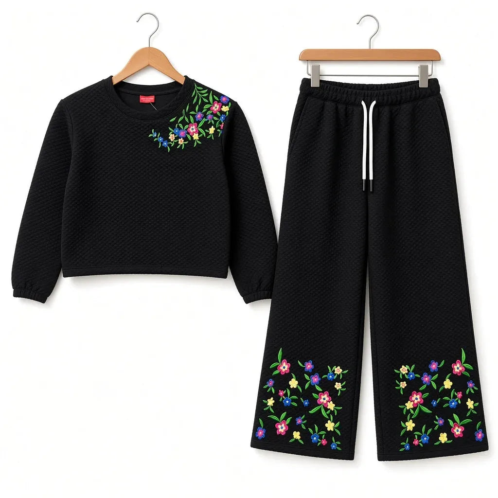 A two-piece girls' outfit set consisting of a black cropped long-sleeve top and matching wide-leg pants, both featuring colorful floral embroidery. The top has embroidery on the left chest, and the pants have matching embroidery on the lower legs.