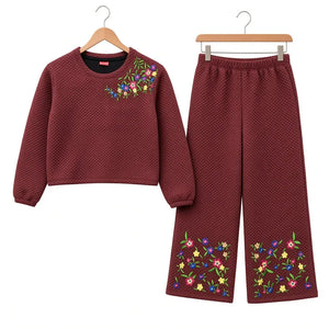 A two-piece children's outfit set consisting of a long-sleeve cropped sweater and matching wide-leg pants, both in a textured deep burgundy fabric with colorful floral embroidery accents, displayed on wooden hangers against a white background.